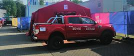 Na zdjęciu widoczny samochód pożarniczy osobowy Ford, w tle ścianki wspinaczkowe do rozgrywania konkurencji sportowych, oraz namiot sztabowy strażaków