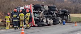 Samochód ciężarowy na boku a obok niego strażacy.