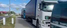 Na pierwszym planie (od prawej): oznakowany furgon mazowieckiej Inspekcji Transportu Drogowego i stojące za nim dwa ciągniki siodłowe z podpiętymi naczepami. W tle: wiadukt nad drogą ekspresową i stacja paliw.