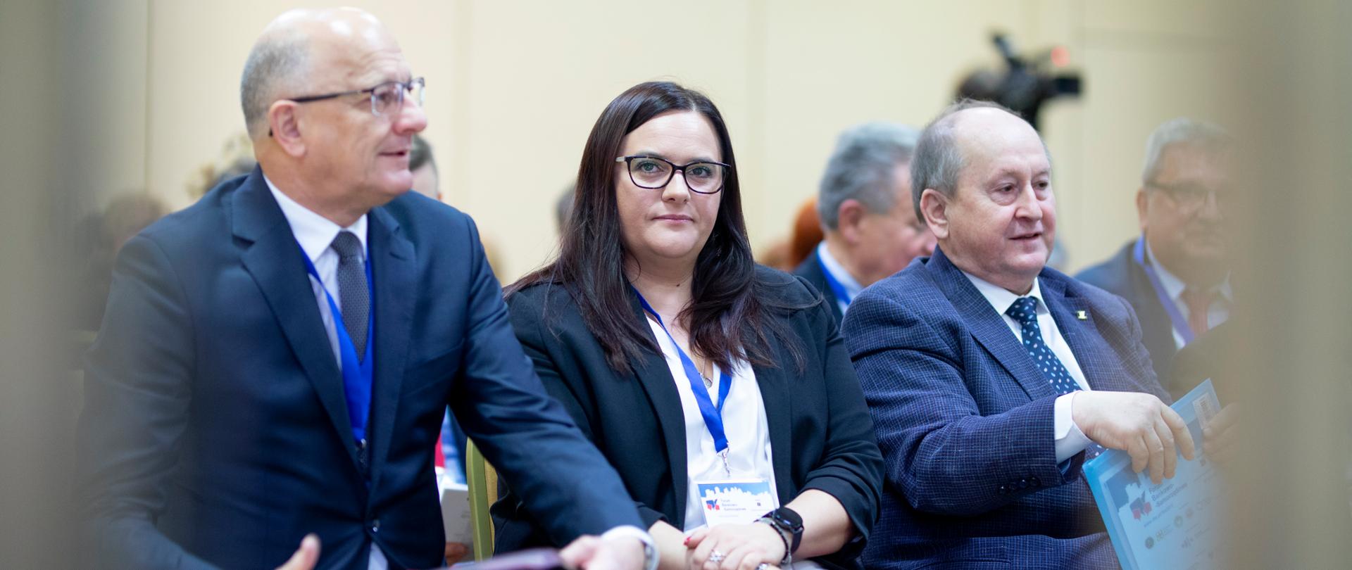 Trzy osoby - dwóch mężczyzn i kobieta - siedzą na krzesłach ustawionych w rzędzie. Pośrodku minister Małgorzata Jarosińska-Jedynak.