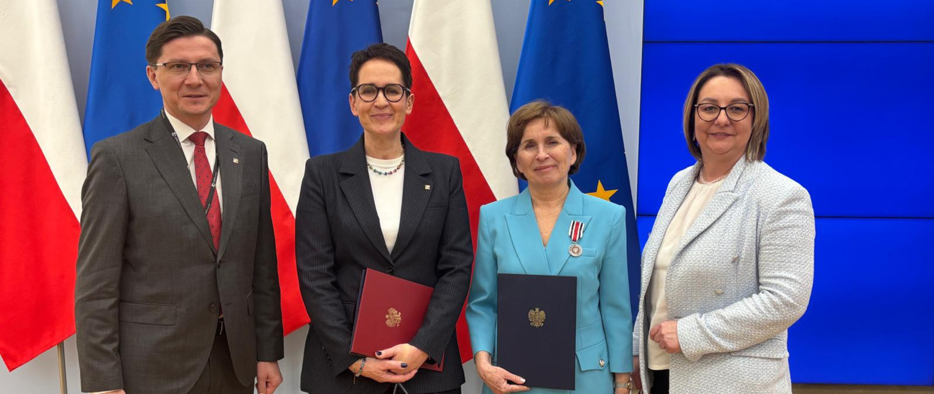 Zdjęcie pamiątkowe, cztery osoby na tle flag polskiej i unijnej