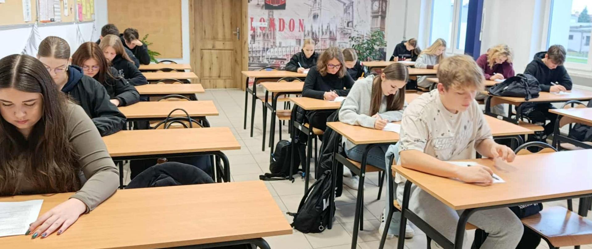 Uczniowie siedzą w klasie i rozwiązują test.