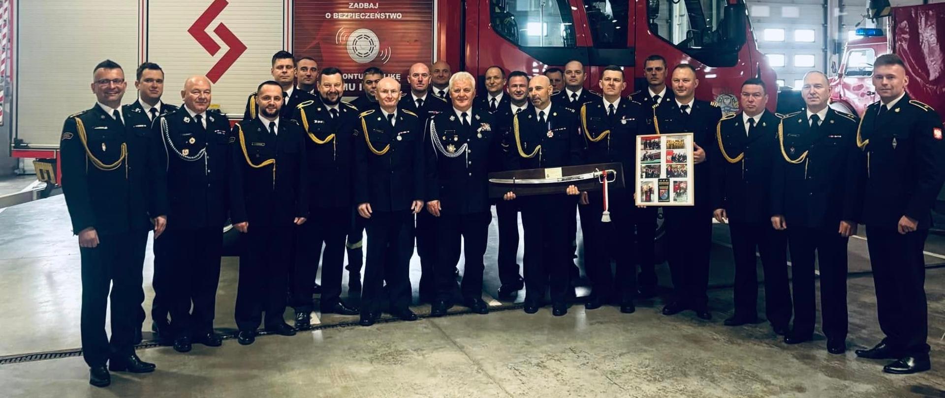 Grupowie zdjęcie pamiątkowe uczestników uroczystości. Strażacy zgromadzeni na garażu jednostki na tle wozu pożarniczego 