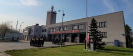 Strażacy podczas uroczystej zmiany służby na której podniesiono flagę na maszt. Strażacy na tle budynku Komendy Miejskiej Państwowej Straży Pożarnej w Tychach