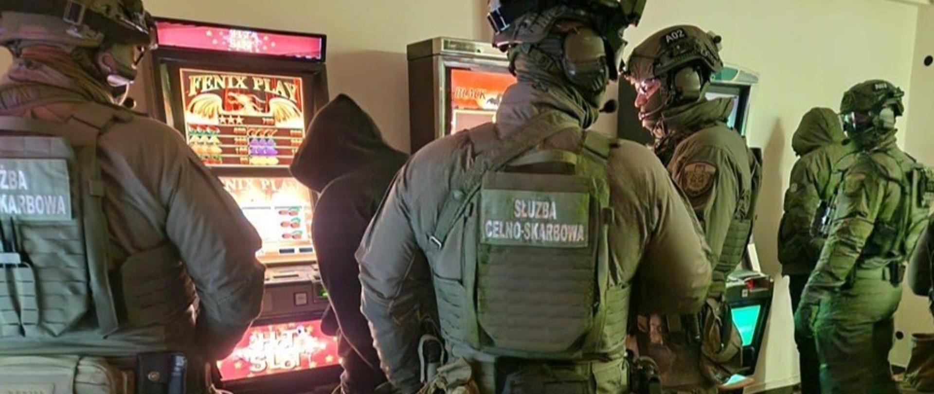 Funkcjonariusze Służby Celno‑Skarbowej prowadzą czynności przy automatach do gier w lokalu.
