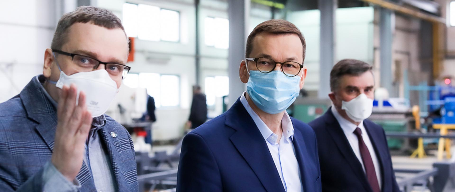 Premier oraz dwóch mężczyzn idą w siedzibie firmy.