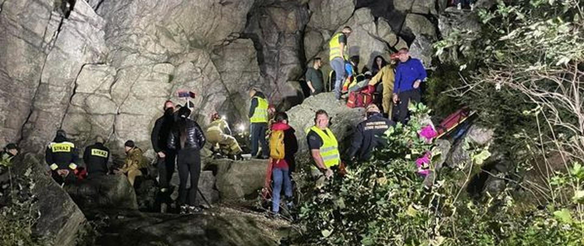 Uczestnicy ćwiczeń stoją na skałach. Jest noc