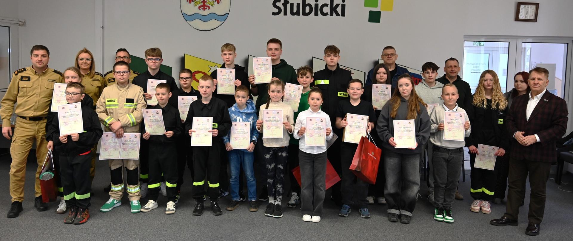 Zdjęcie grupowe uczestników i opiekunów na tle ściany z napisem Powiat Słubicki. 