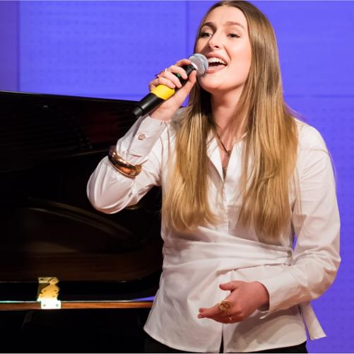 Zdjęcie przedstawia śpiewającą uczennicę ZPSM stojącą przy fortepianie