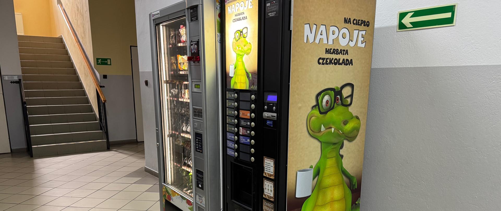 Zdjęcie przedstawiające automaty z przekąskami i ciepłymi napojami, które znajdują się na korytarzu w szkole.
