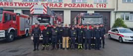 Zdjęcie grupowe strażaków stojących na placu przed bramami wyjazdowymi.