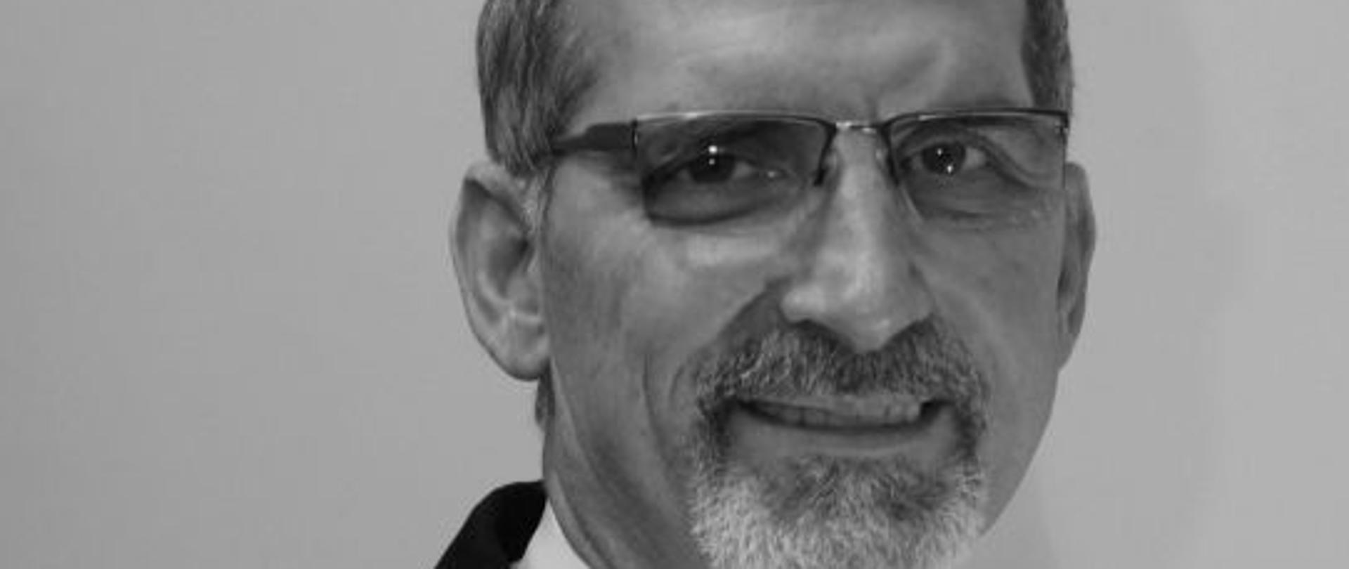 czarno-białe zdjęcie strażaka w mundurze w białej koszuli z krawatem, w okularach z brodą i wąsem