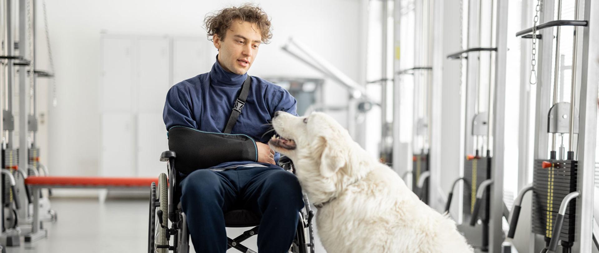 Zdjęcie przedstawia mężczyznę na wózku inwalidzkim z psem