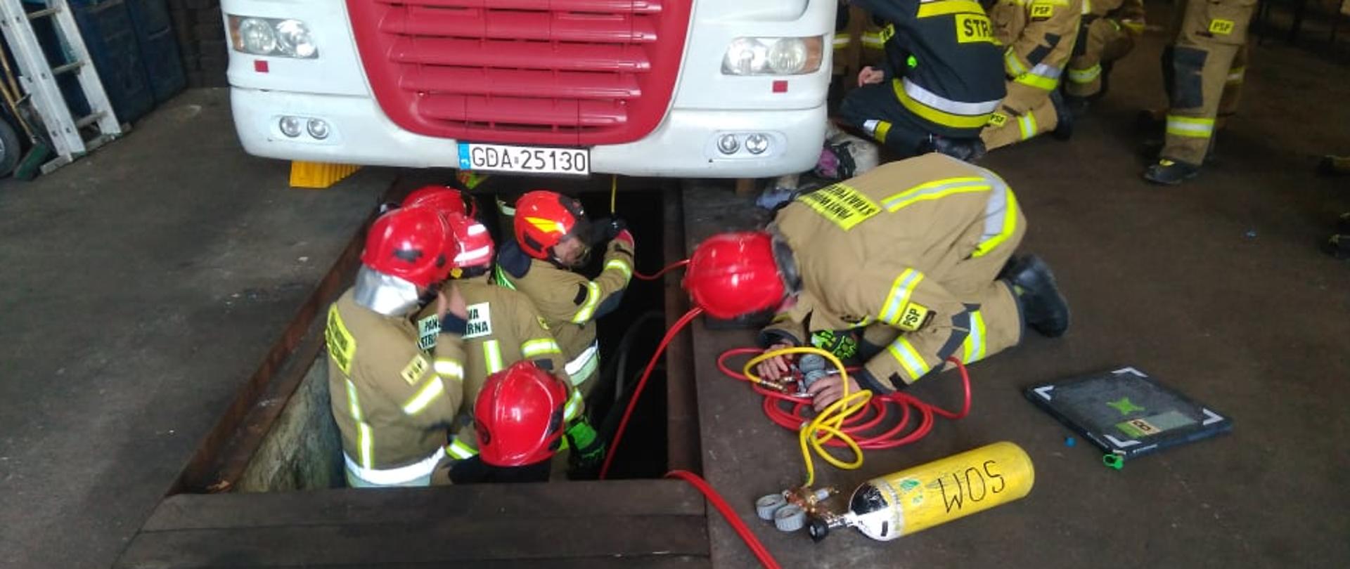 Zdjęcie przedstawia strażaków podczas próby podnoszenia ciągnika siodłowego z użyciem poduszek pneumatycznych