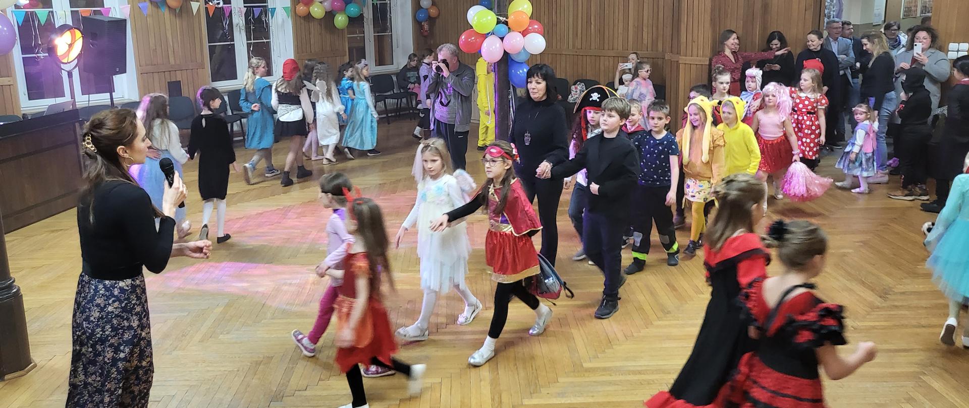 Grafika przedstawiająca grupę bawiących się uczniów oraz przystrojoną sale, podczas zabawy karnawałowej