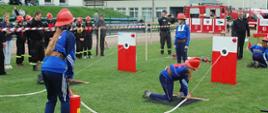 Zdjęcie przedstawia zawodników MDP podczas konkurencji ćwiczenie bojowe. Na pierwszym planie trwa pompowanie wody z hydronetek do nalewaków. Z lewej strony zdjęcia widoczni są zawodnicy i kibice obserwujący zmagania.