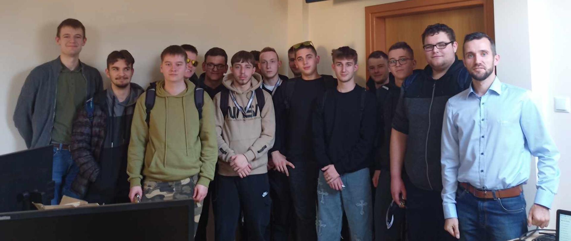 Zdjęcie grupowe uczestników szkolenia i instruktora w sali wykładowej. Grupa stoi pod dużym ekranem, na którym wyświetlony jest interfejs programu do zarządzania gospodarstwem.