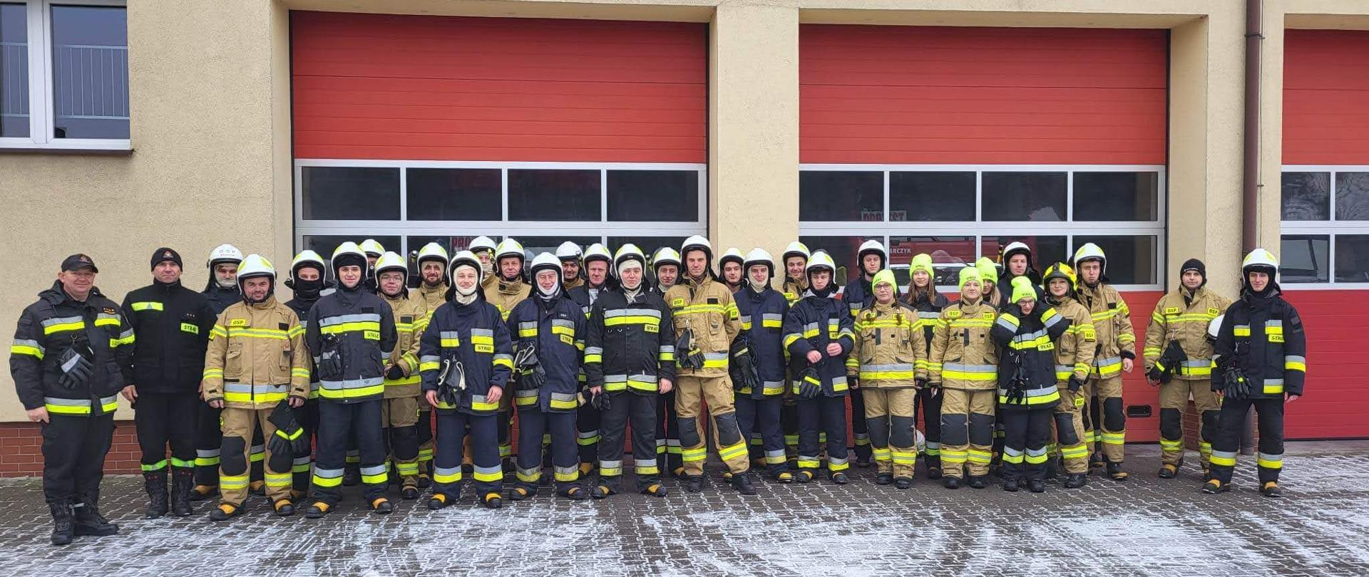 Zdjęcie grupowe uczestników kursu podstawowego strażaków ratowników ochotniczych straży pożarnych na tle garaży Jednostki Ratowniczo - Gaśniczej w Krotoszynie. 