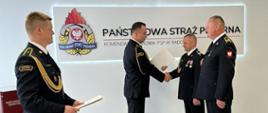 Mężczyźni w umundurowaniu wyjściowym. Komendant ściska rękę jednego z dwóch emerytów (strażaka).