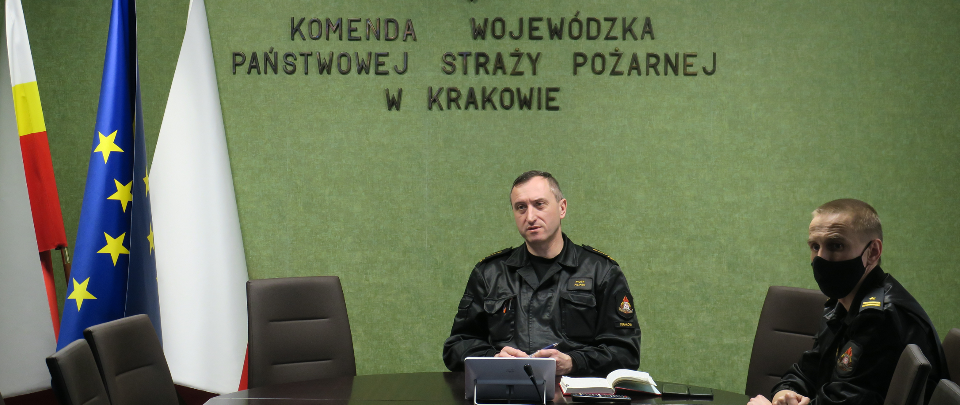 Małopolski Komendant Wojewódzki PSP wraz z Zastępcą siedzą przy stole na sali konferencyjnej. Przed nimi leżą notatki. Ubrani są w mundury dowódczo- sztabowe.