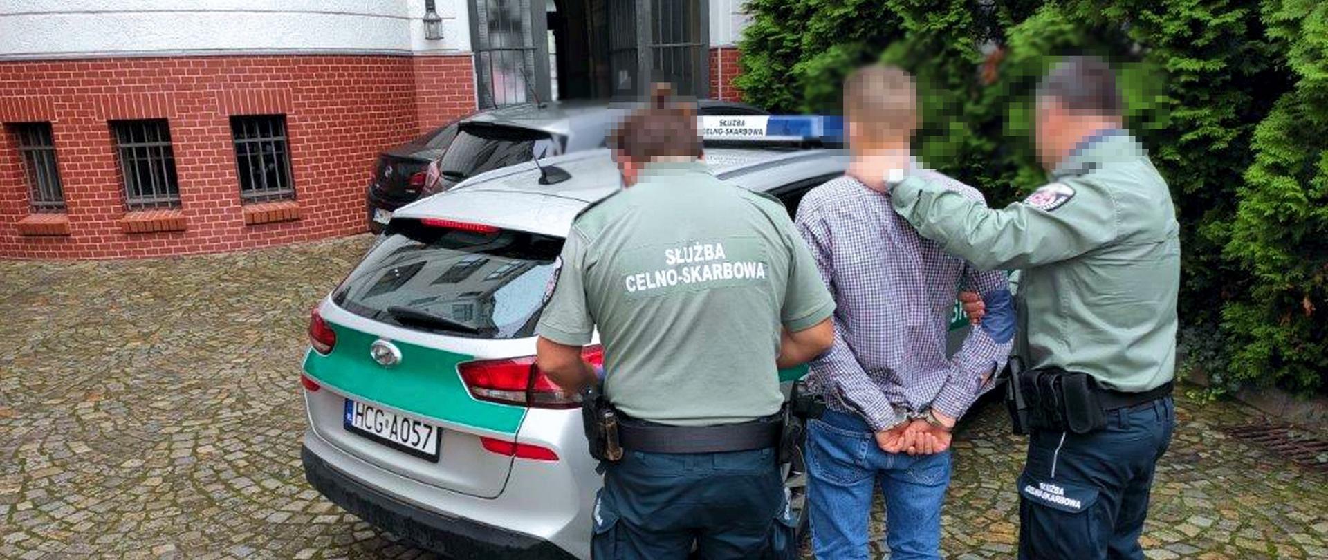 Funkcjonariusze KAS prowadzą zatrzymanego do radiowozu