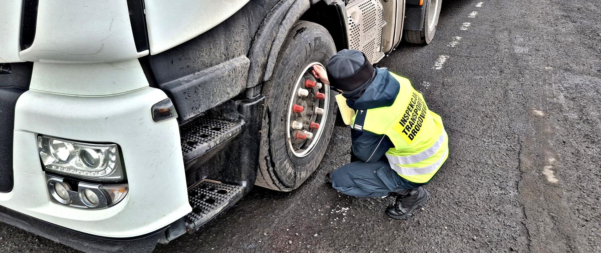 Inspektor w charakterystycznej żółtej kamizelce z napisem „INSPEKCJA TRANSPORTU DROGOWEGO” dokonuje oględzin koła ciągnika siodłowego