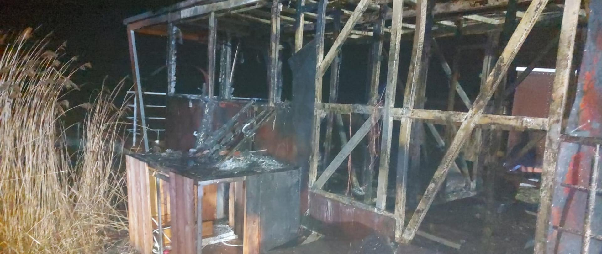 Zdjęcie przedstawia spalony domek pływający. Został sam szkielet budynku. 
