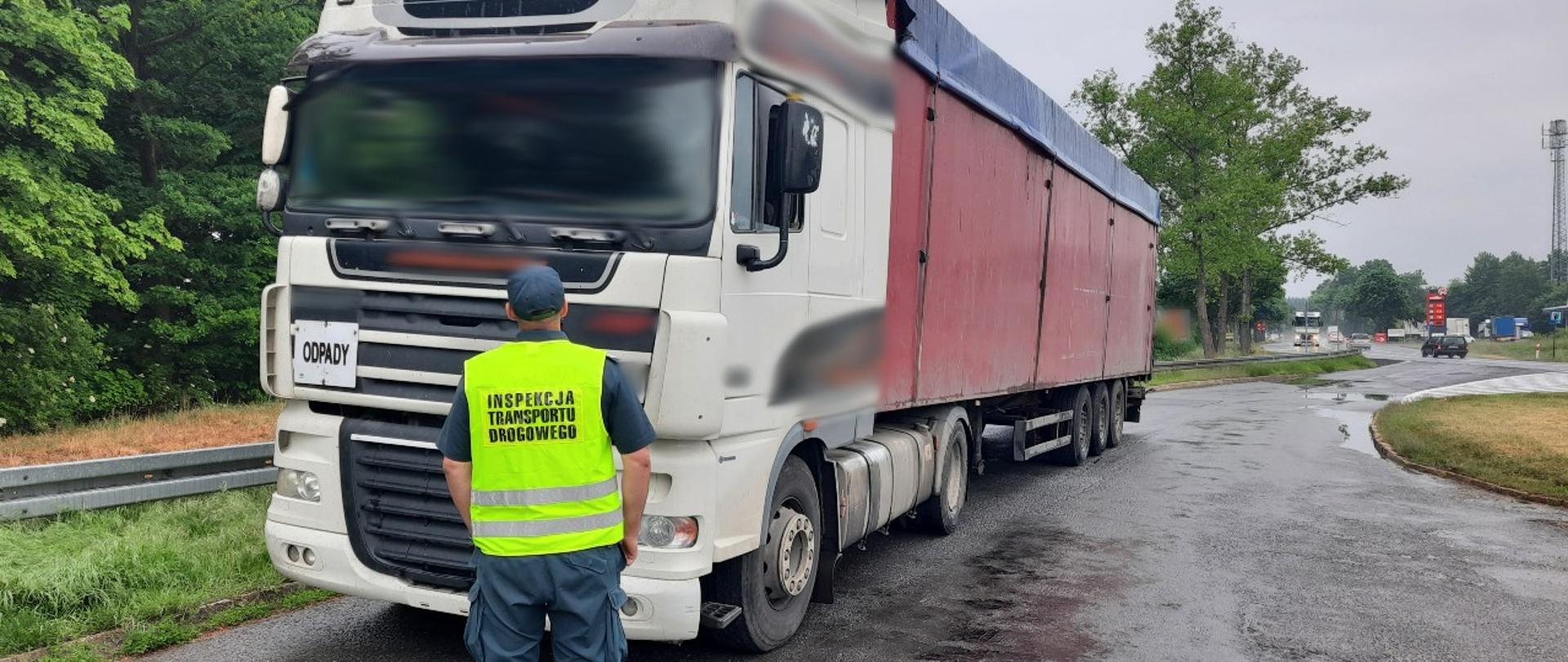 Inspektor dolnośląskiej ITD stoi przed zatrzymanym do kontroli drogowej zestawem ciężarowym.