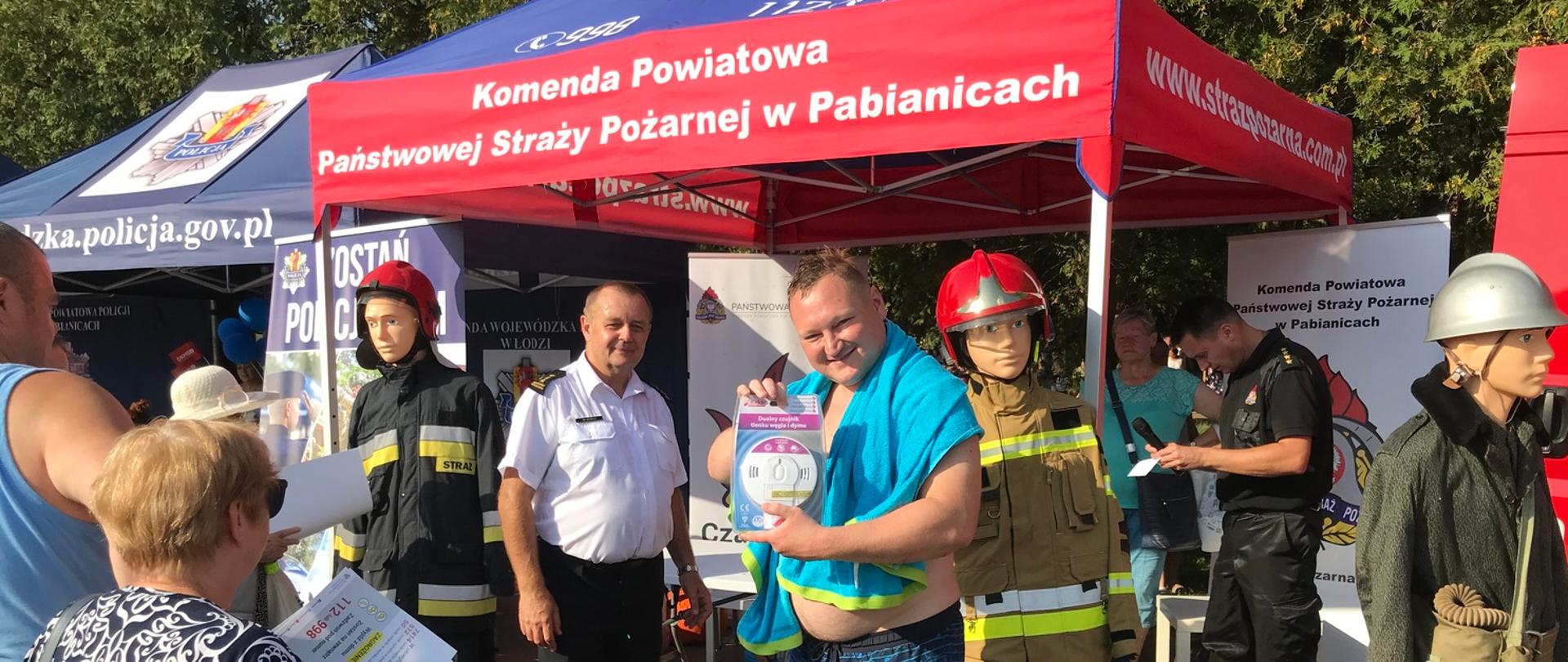 Na stoisku KP PSP w Pabianicach komendant powiatowy wręcza zwycięzcom konkursu dualne czujki tlenku węgla i dymu.