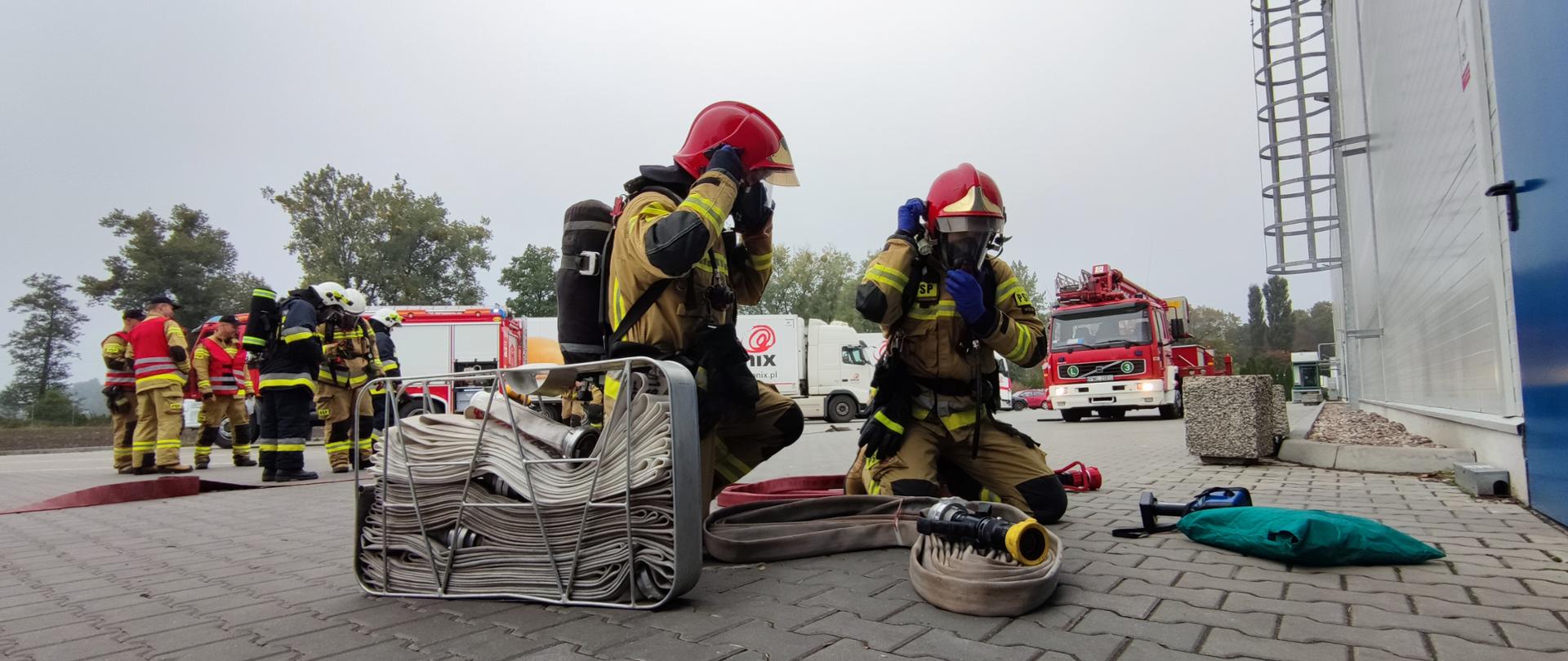 STRAŻACY ZE SPRZĘTEM PRZYGOTOWUJĄ SIĘ DO WEJŚCIA DO OBIEKTU