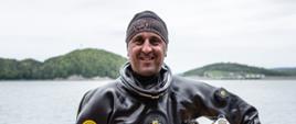 Na zdjęciu Zastępca Podkarpackiego Komendanta Wojewódzkiego st. bryg. Daniel Dryniak stojący na brzegu jeziora Solińskiego, ubrany w skafander przeznaczony do pracy w wodach skażonych i zanieczyszczonych trzymający hełm z podpiętą wiązką przewodową pod pachą