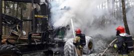 Zdjęcie przedstawia palącą się maszynę leśną Timberjack. Rota strażaków operuje prądem piany ciężkiej na pożar. 