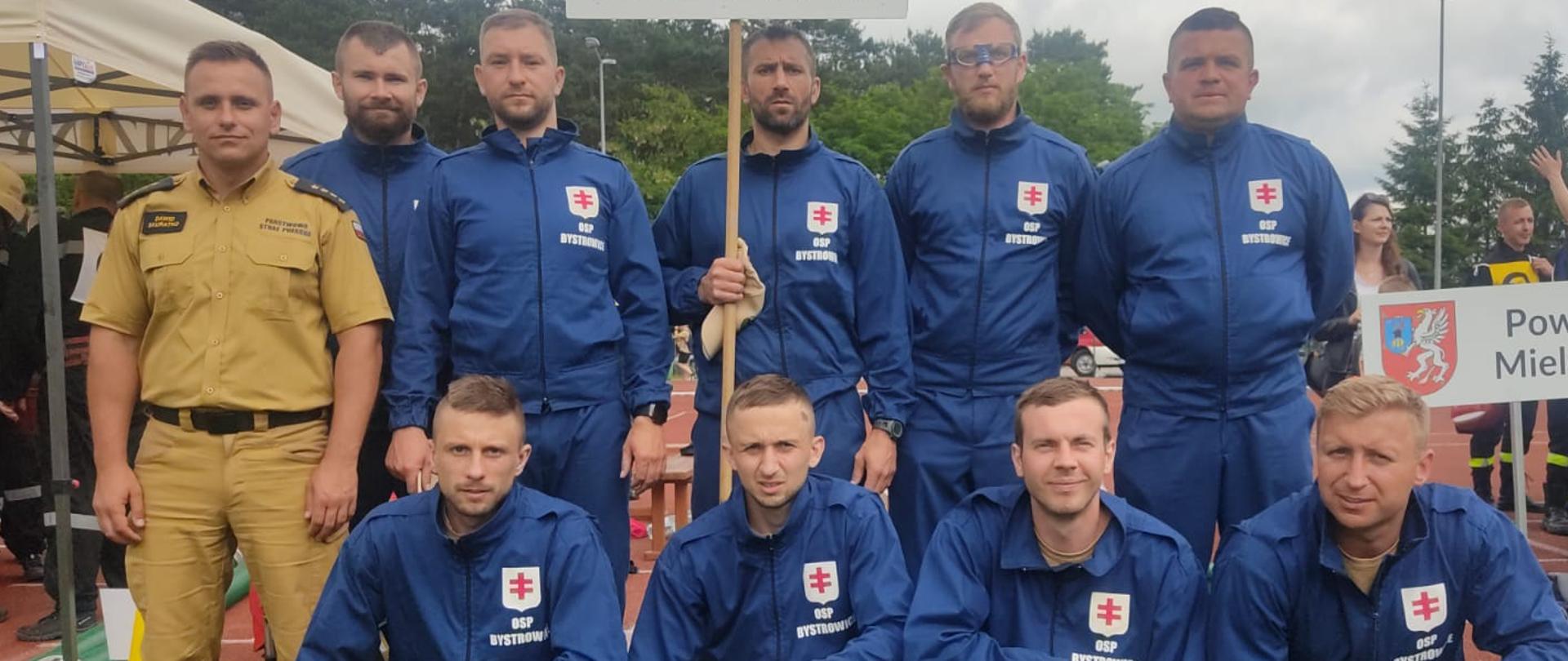 Na zdjęciu drużyna OSP Bystrowice ustawiona do zdjęcia grupowego wraz z opiekunem drużyny. Wszyscy ubrani są w umundurowanie koszarowe.