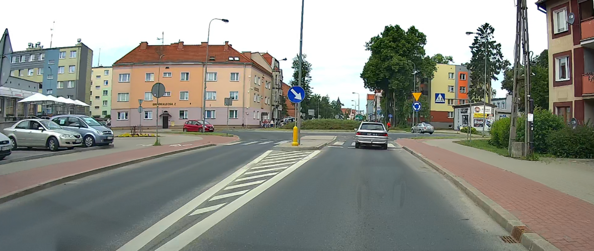 Ulica w centrum miasta. Na pierwszym planie przejście dla pieszych. W tle bloki mieszkalne.