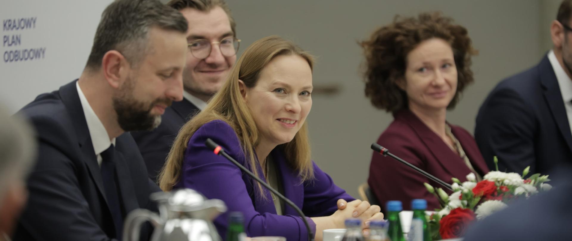 Cztery osoby siedzą obok siebie przy stole. Druga od lewej uśmiechnięta siedzi minister Katarzyna Pełczyńska-Nałęcz. 