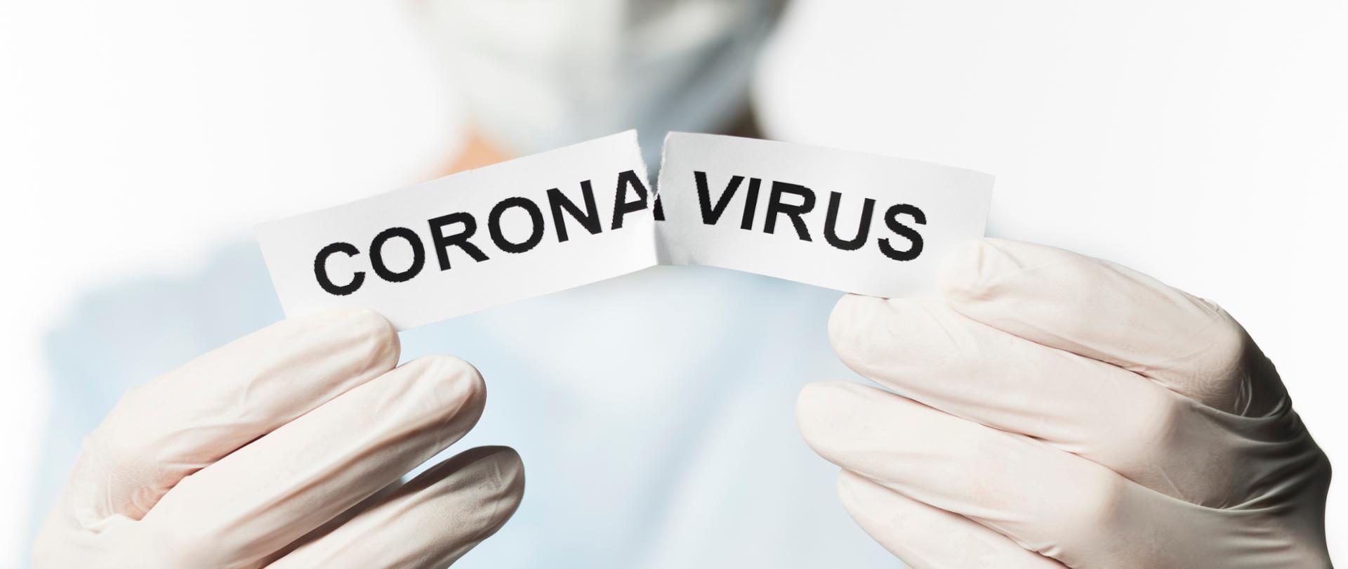 Dłonie w rękawiczkach przedzierające na pół karteczkę z napisem Coronavirus