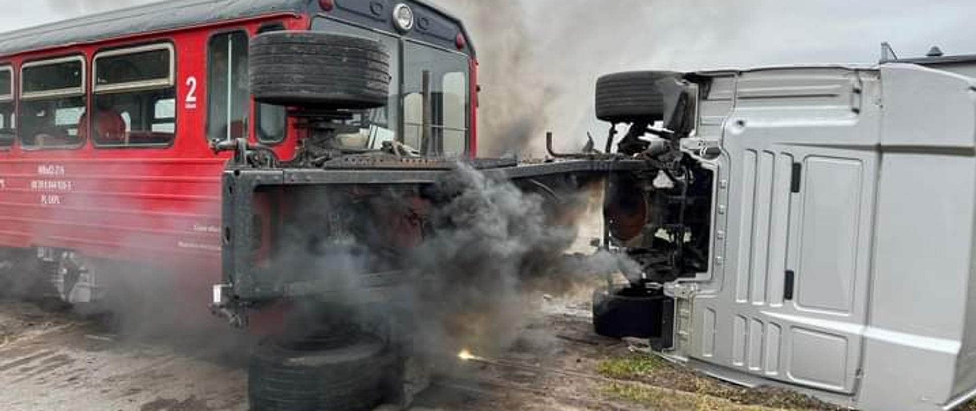 Zdjęcie przedstawia pozorowane zderzenie pociągu z samochodem ciężarowym na przejeździe kolejowym. Samochód ciężarowy jest przewrócony na prawy bok.