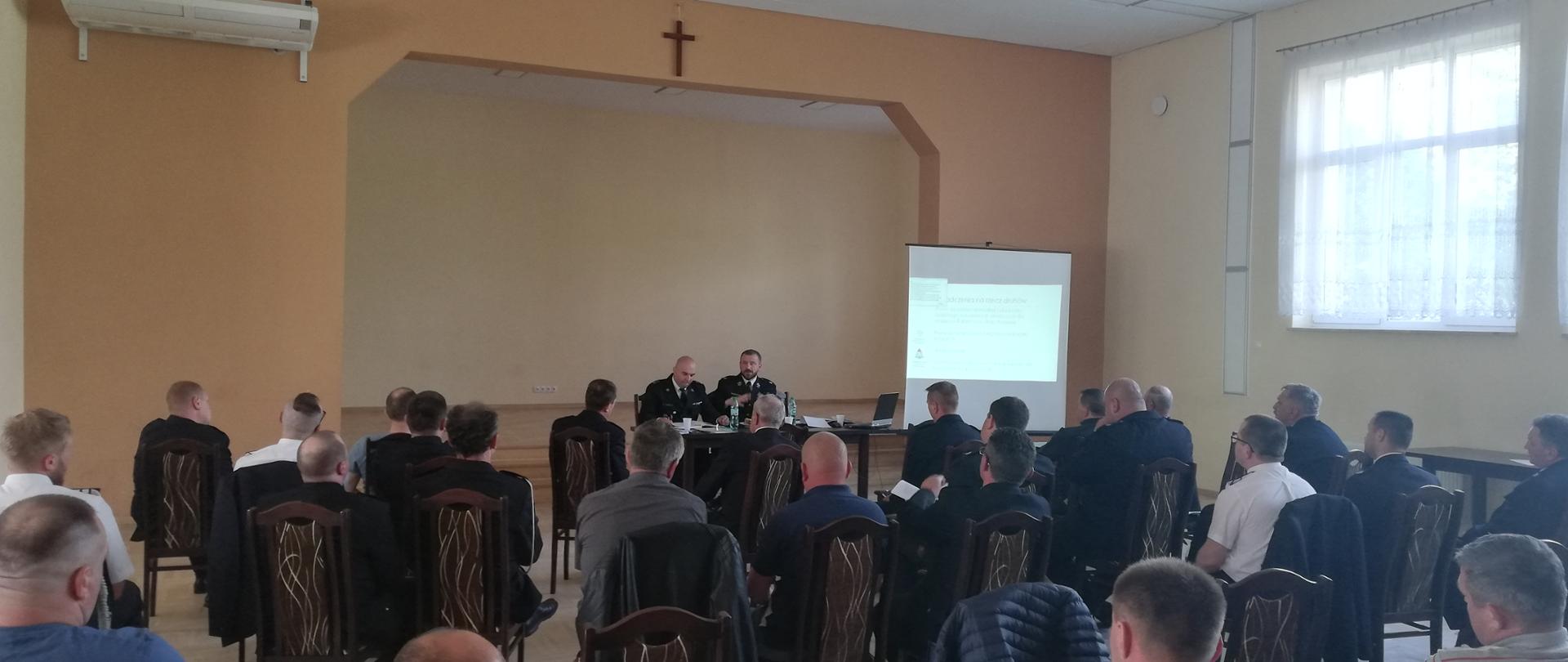 Zdjęcie przedstawia osoby siedzące na sali w trakcie prowadzonych konsultacji społecznych projektu Ustawy o Ochotniczej Straży Pożarnej. 