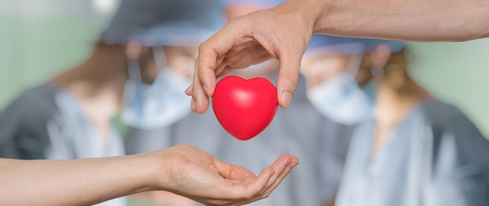 Czerwone serce trzymane palcami ręki i przekazywane do drugiej otwartej dłoni.