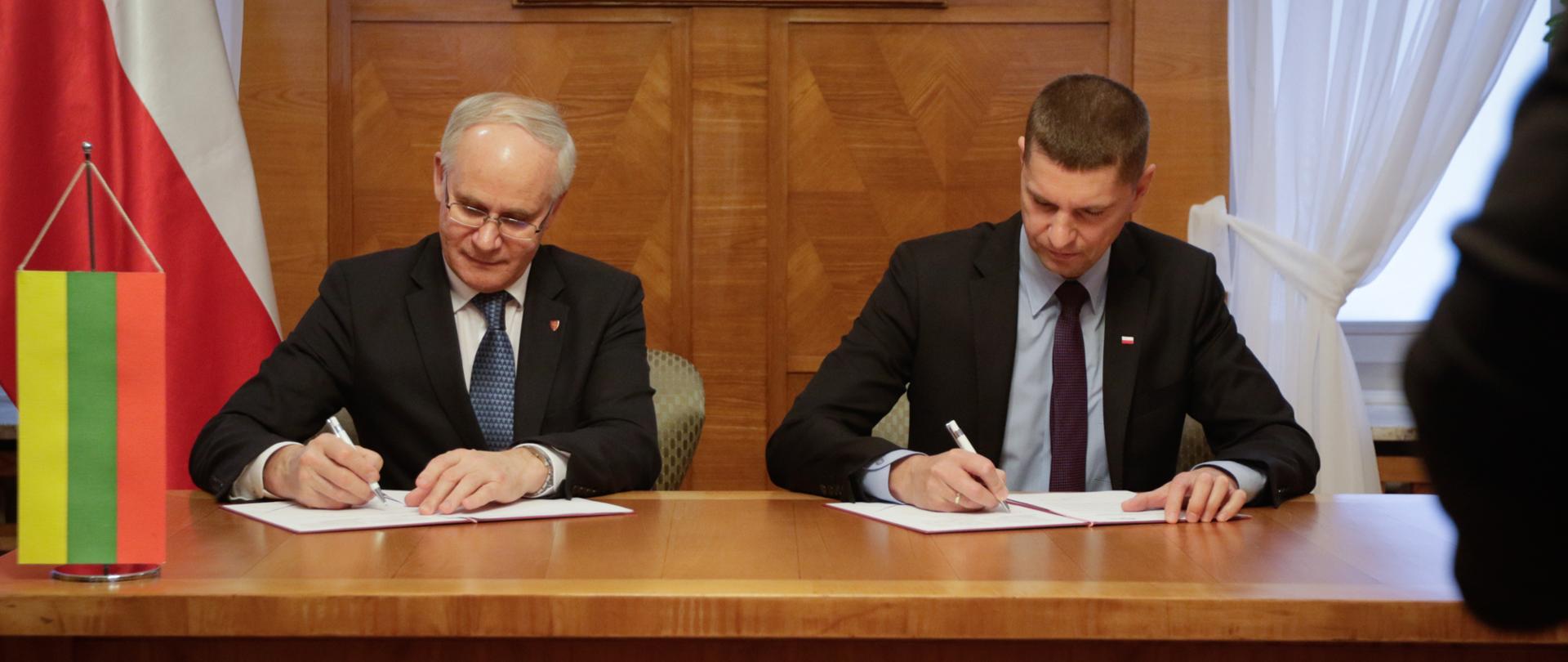 Ministrowie podpisuje deklarację. Na stole flaga Polski i Litwy. 