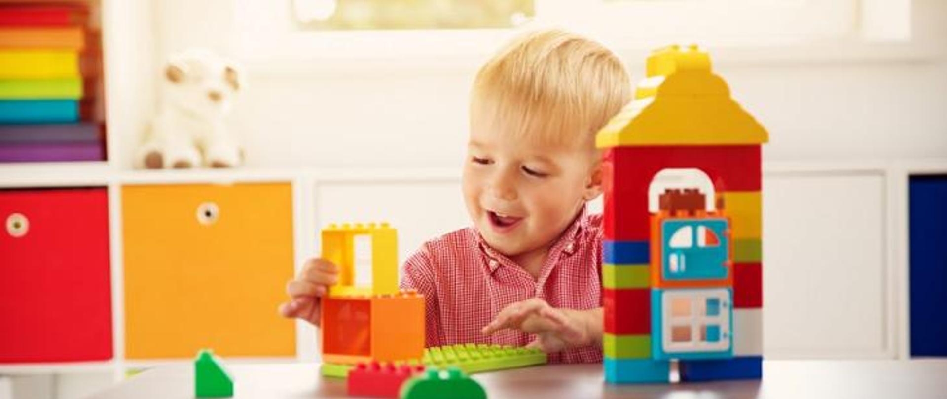 Małe uśmiechnięte dziecko bawi się kolorowymi klockami w przedszkolu