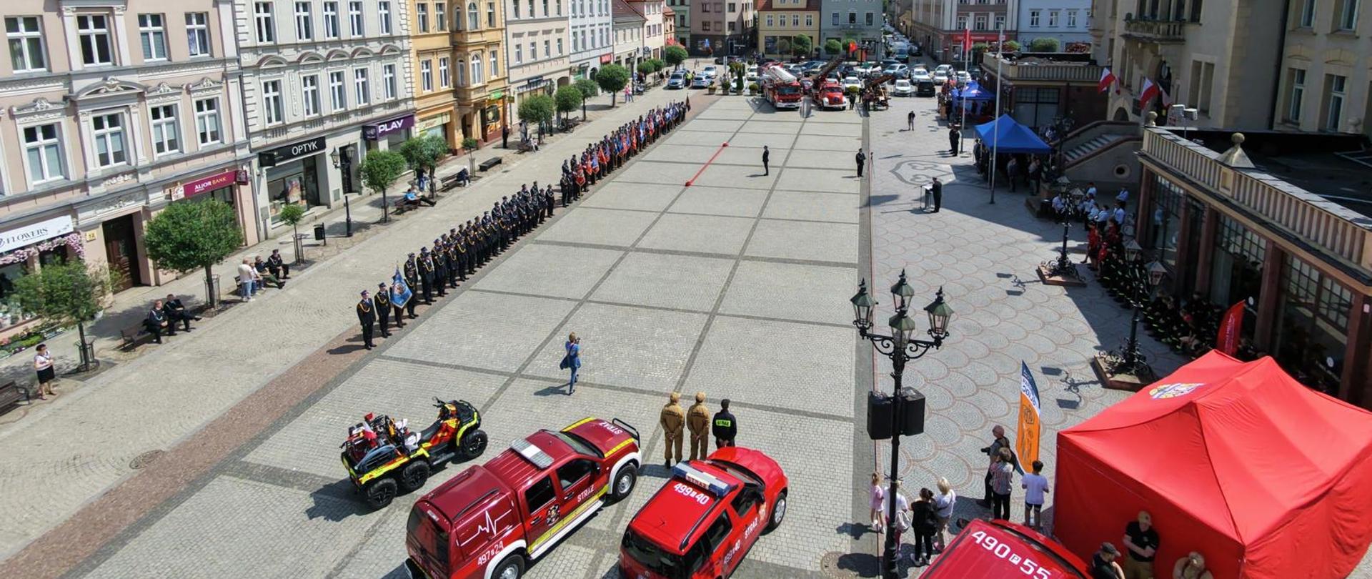 Na krotoszyńskim rynku odbywają się obchody Dnia Strażaka. Pododdziały i poczty sztandarowe ustawione w zwartej kolumnie oczekują na rozpoczęcie uroczystości. Zdjęcie wykonane z drona. 