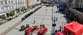 Na krotoszyńskim rynku odbywają się obchody Dnia Strażaka. Pododdziały i poczty sztandarowe ustawione w zwartej kolumnie oczekują na rozpoczęcie uroczystości. Zdjęcie wykonane z drona. 