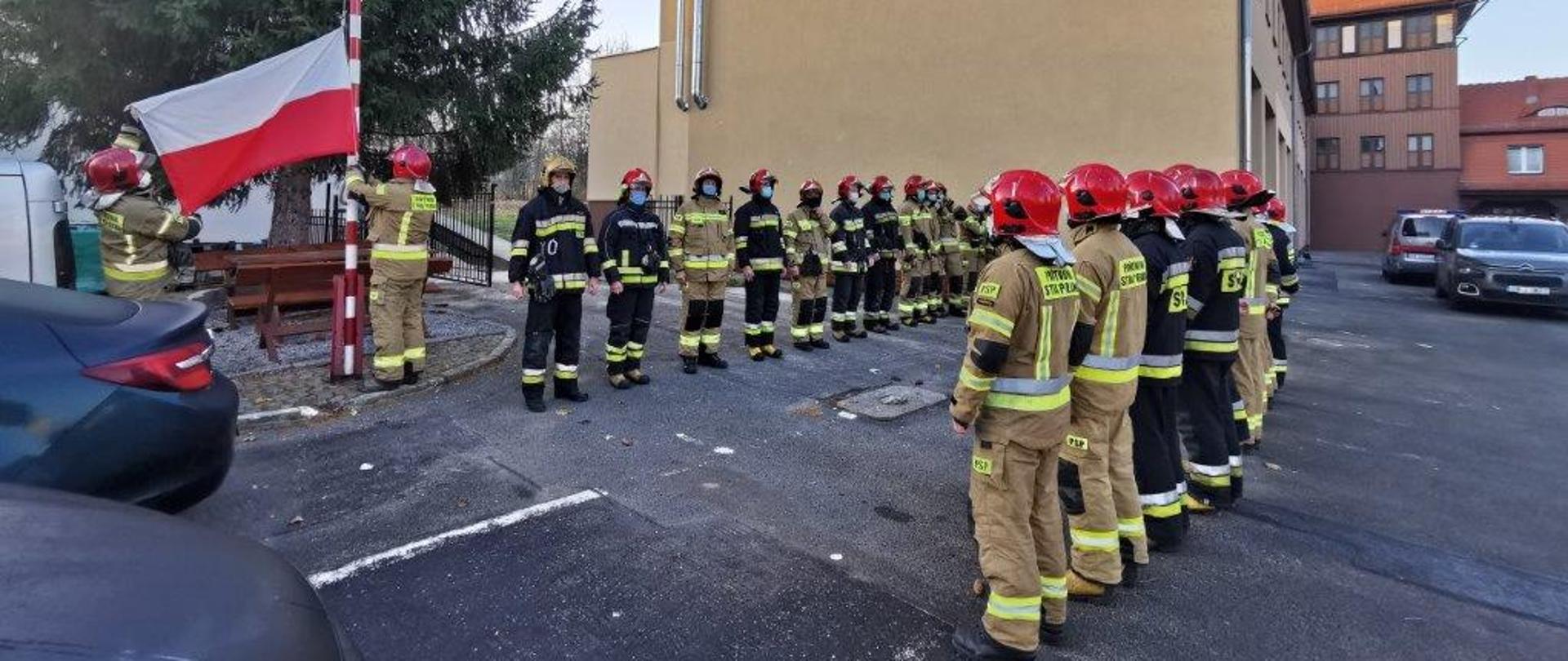 strażacy w mundurach bojowych w kolorze piaskowym oraz granatowym, na głowach mają czerwone hełmy stoją na placu jednostki ratowniczo gaśniczej nr 1 w Wałbrzychu