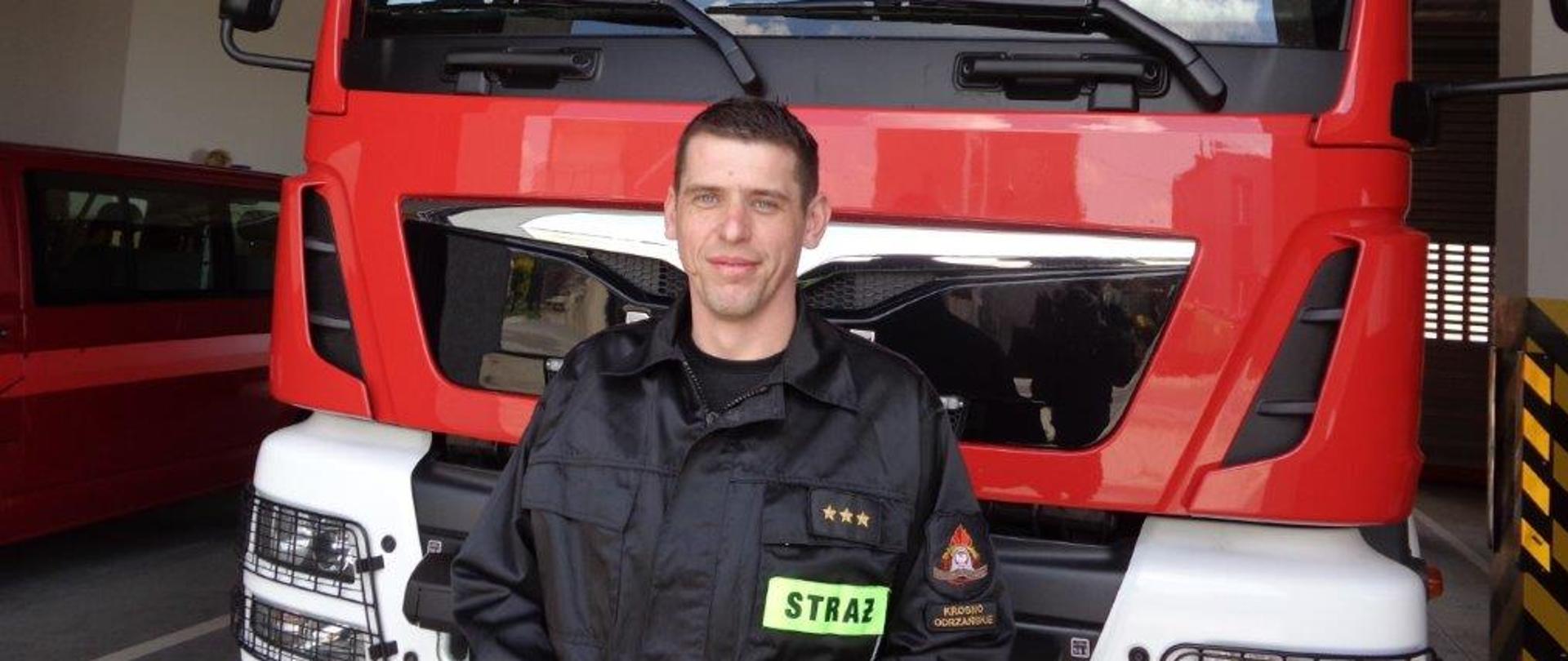 Na zdjęciu widać strażaka na tle pojazdu pożarniczego.