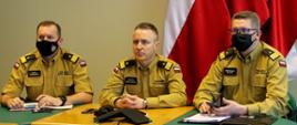 Po lewej stronie zastępca komendanta głównego PSP nadbryg. Adam Konieczny, następnie komendant główny PSP, nadbryg. Andrzej Bartkowiak, po prawej stronie zastępca KG PSP nadbryg. Krzysztof Hejduk. Wszyscy trzej siedzą przy stole podczas wideokonferencji, ubrani są w nowe umundurowanie służbowe koloru "musztardowego"