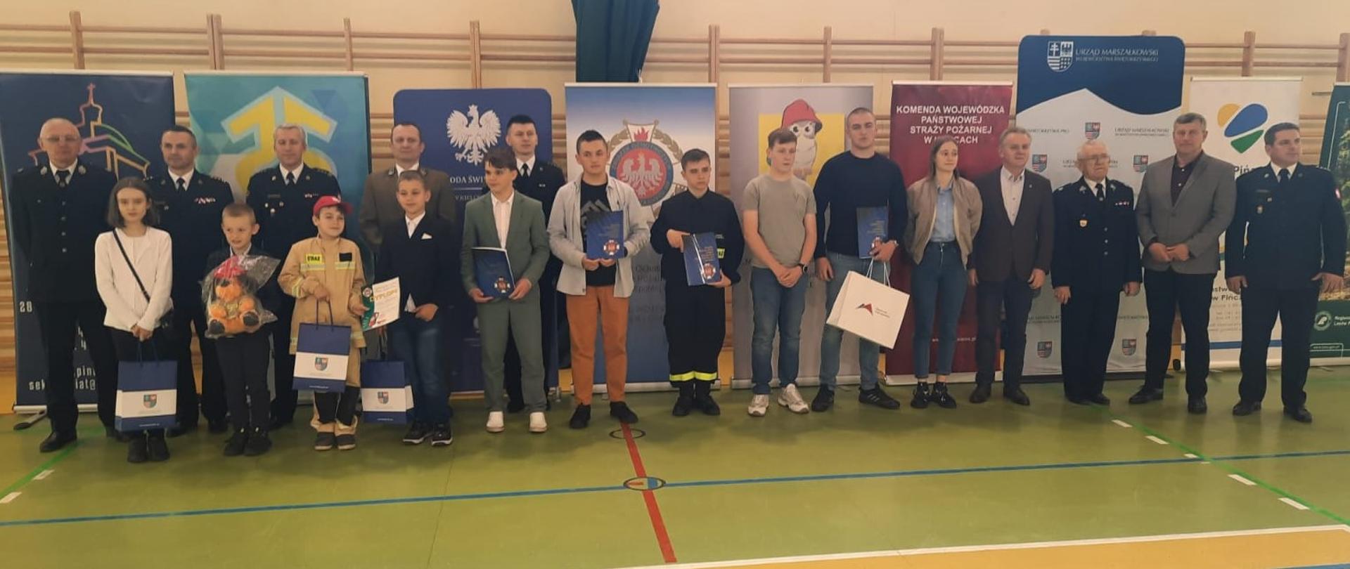 W pomieszczeniu stoją w szeregu strażacy ubrani w mundury wyjściowe oraz uczestnicy konkursu w grupie wiekowej trzeciej OTWP.
