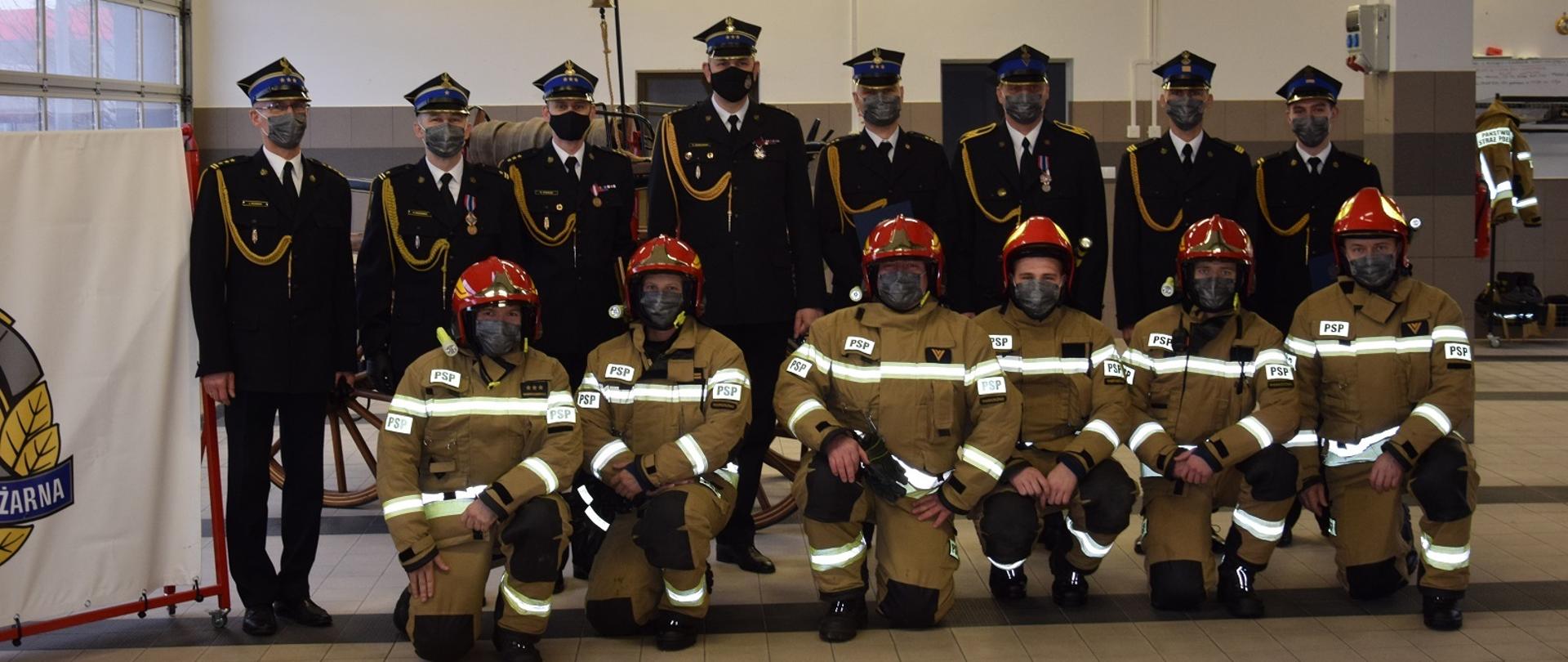 Na zdjęciu wyróżnieni strażacy ustawieni w dwuszeregu, pierwszy rząd złożony ze zmiany służbowej klęczy w ubraniach bojowych, drugi stoi. Po lewej stronie stoi komendant powiatowy PSP w Wąbrzeźnie, na środku stoi zastępca kujawsko-pomorskiego komendanta wojewódzkiego PSP.