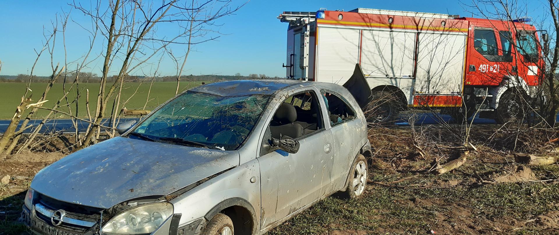 Samochód osobowy, w stanie po wypadku. Za nim pojazd straży pożarnej.