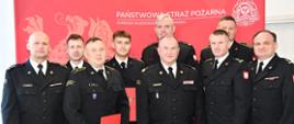 9 strażaków w mundurach wyjściowych stoi do zdjęcia, część z nich teczki w rękach.